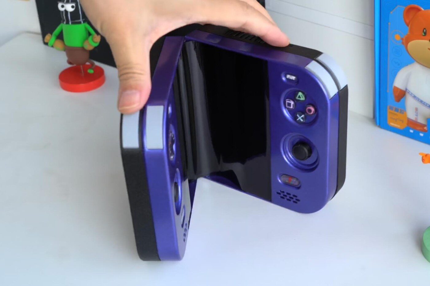 Hand holding the custom foldable PlayStation 2 Duo handheld, half open, in purple